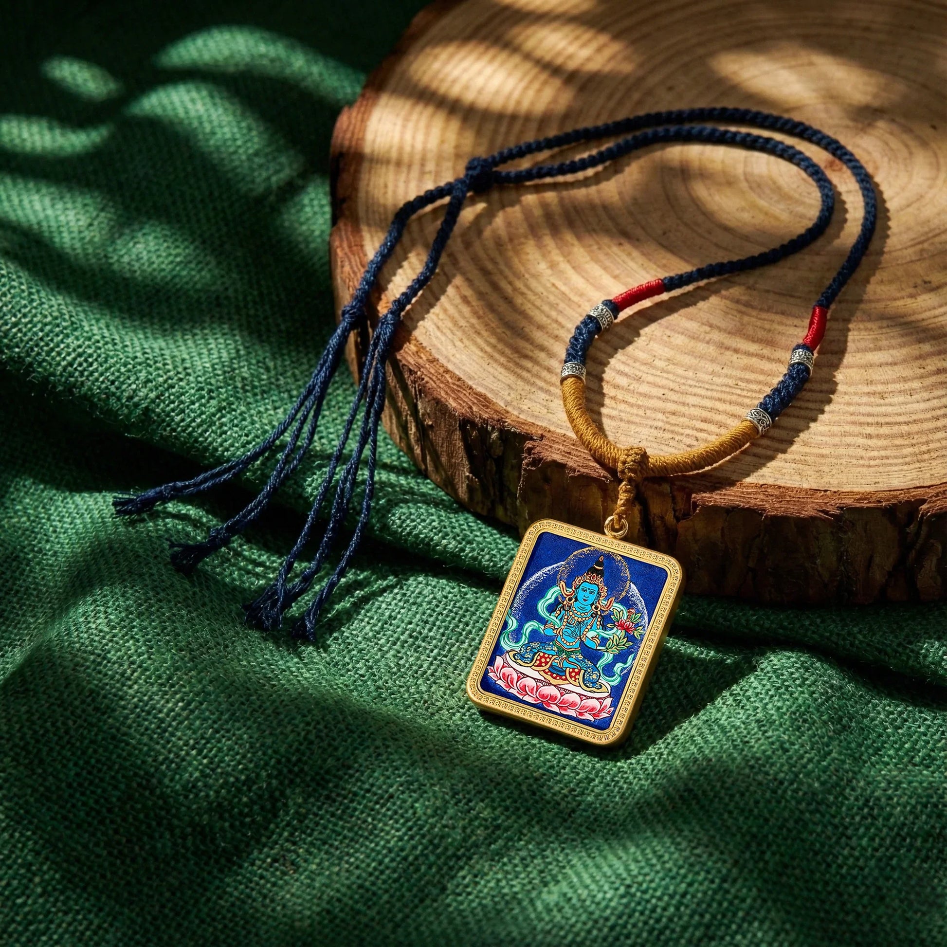 Handcrafted Buddhist deity pendant necklace with woven cord on green fabric background